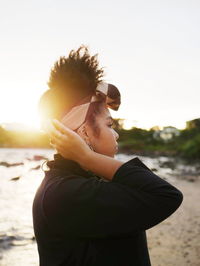 Side view of man wearing sunglasses standing against sky during sunset