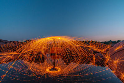 Reflection of man spinning wire wool on land in lake against clear sky at night