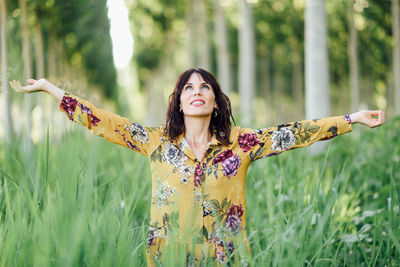 Portrait of young woman with arms outstretched standing on field