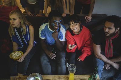 Male and female using smart phone while sitting with friends on sofa at home