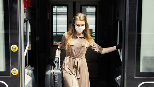 Woman wearing mask with suitcase exiting from train