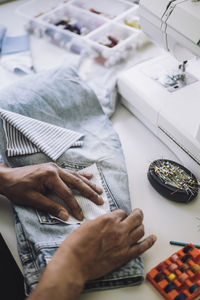 High angle view of fashion designer pinning fabric on back pocket of jeans at workshop