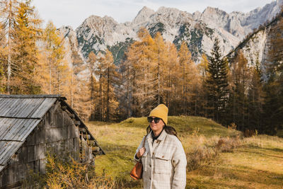 Portrait of young woman walking on meadow with golden larch trees under mountains