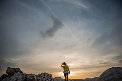 Rear view of woman wearing hat while standing on rocks against sky