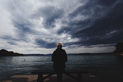 Woman standing by sea against sky during sunset