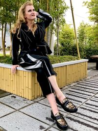 Full length of young woman sitting on railing against trees