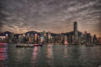 Illuminated buildings by river against sky at dusk in hong kong 
