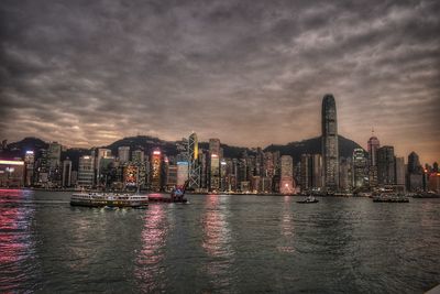 Illuminated buildings by river against sky at dusk