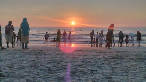 People at beach against sky during sunset