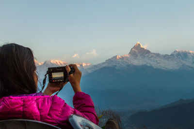 Rear view of man photographing mountains against clear sky