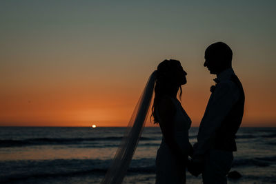 Silhouette couple on beach against sky during sunset