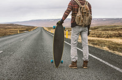 Low section of man standing with skateboard on highway