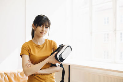 Portrait of female entrepreneur holding virtual reality simulator while standing by window