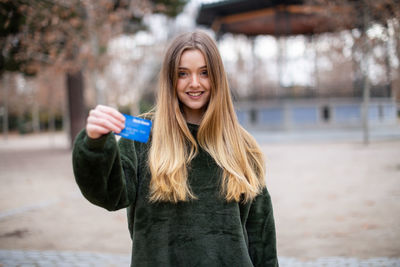 Portrait of woman holding credit card while standing in park
