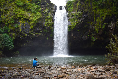 Rear view of boy standing against waterfall