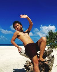 Man gesturing while sitting on driftwood at beach