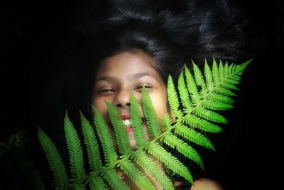 Close-up portrait of smiling teenage girl with fern in dark