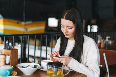 Attractive young brunette smiling woman in casual using mobile phone having brunch in cafe