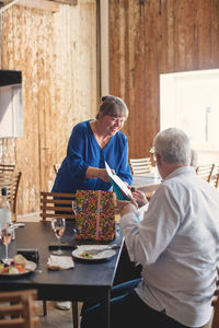 Senior woman giving present to female friend at table in restaurant during lunch party