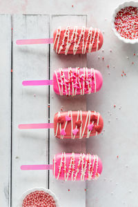 Homemade valentine cakesicles on a white rustic board with bowls of sprinkles.