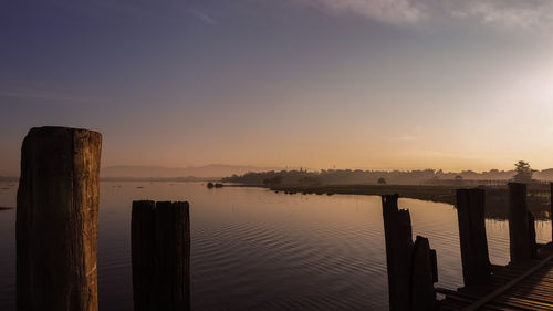 Wooden posts in lake against sky during sunset