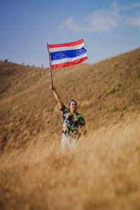 Mature man waving flag while standing on mountain against blue sky