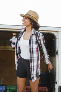 Smiling young woman looking away while standing by van