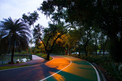 Empty road amidst trees against sky in city