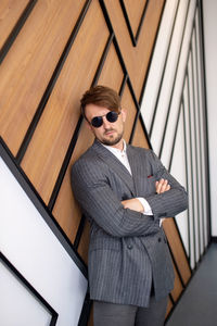 A young man in a suit and sunglasses is standing in a room near the wall