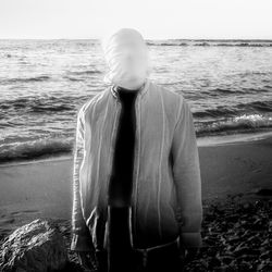 Rear view of man standing at beach against sky