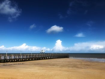 Pier on beach against blue sky