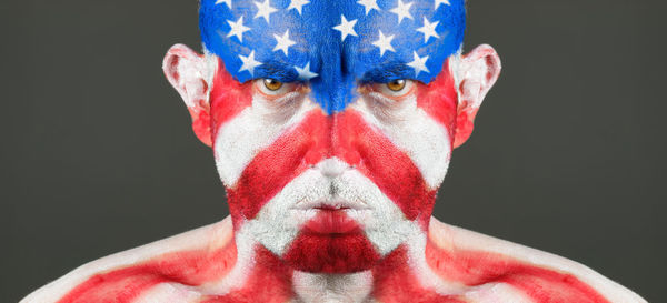 Close-up portrait of sad man with american flag body paint against black background