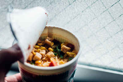 Cropped fingers of person holding food in container by window