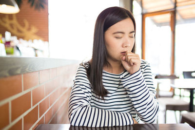 Young woman coughing while sitting in restaurant