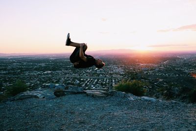 Woman sitting on landscape against sky during sunset