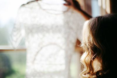 Cropped image of woman holding dress against window