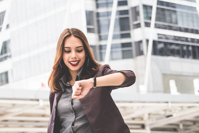 Smiling young businesswoman checking time while standing on elevated walkway 