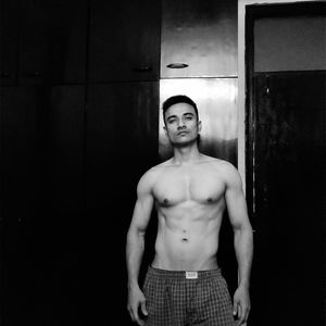 Portrait of shirtless man standing against wall