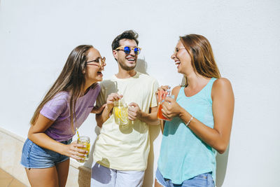 Laughing friends holding refreshing drinks in front of white wall