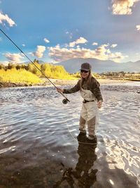 Full length of woman fishing at river against sky