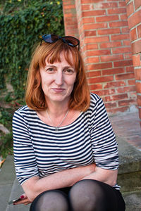 Portrait of smiling woman sitting against brick wall