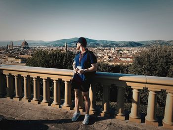 Full length of man sitting on railing in city against sky