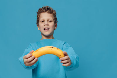 Portrait of young woman holding banana against blue background