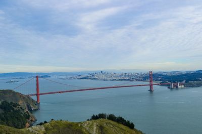 Suspension bridge over sea against cloudy sky