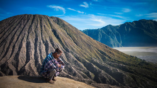 Man sitting on mountain against sky