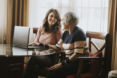 Granddaughter and grandmother smile while using laptop