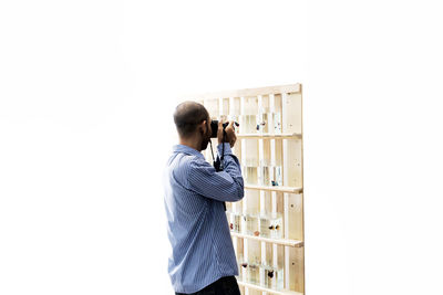 Side view of man photographing fish tanks on shelves against white background