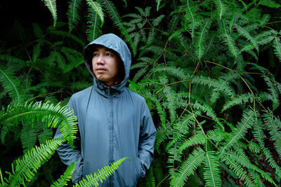 Man in green hoodie with zipper standing in bush of fresh firn leaves