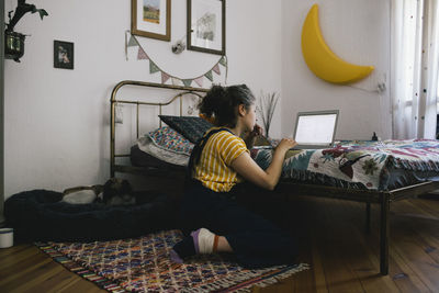 Side view of woman using laptop while sitting in bedroom at home