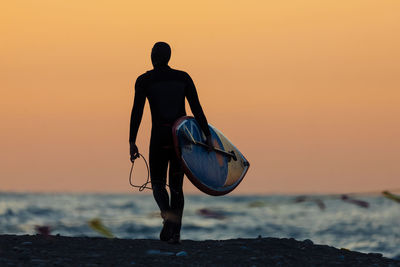 Rear view of man standing on beach during sunset